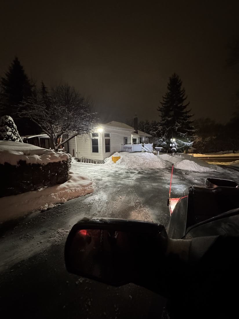 Driveway freshly plowed at night, seen from the cab of the plow truck