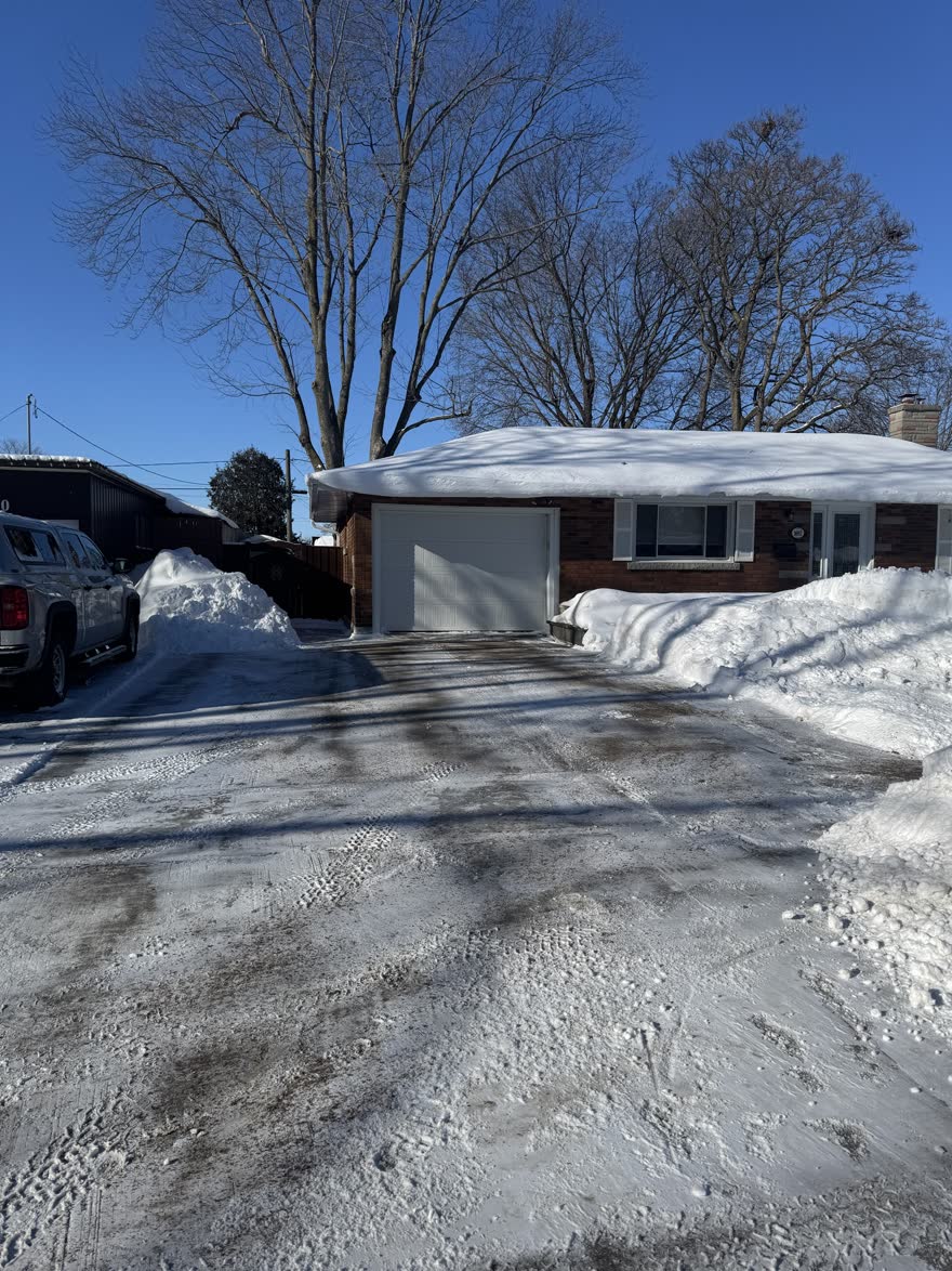 Bungalow driveway cleared to the pavement on a sunny morning with snowbanks stacked beside the garage