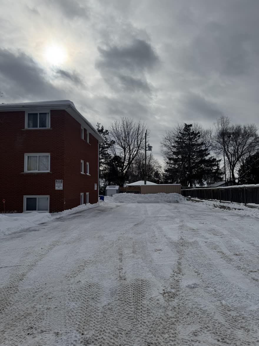 Parking lot behind a three-storey brick apartment building, plowed with the snow piled at the far end