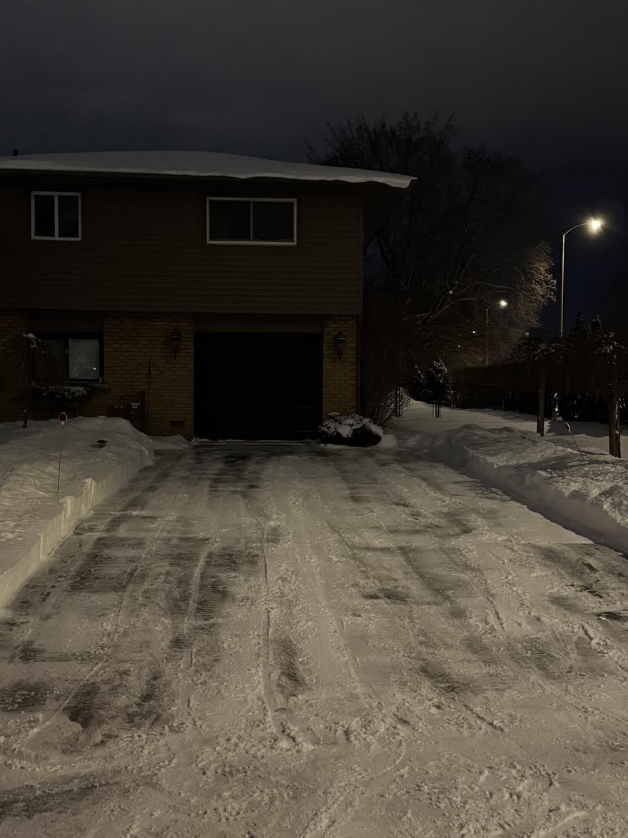 Driveway plowed at night with orange plow stakes marking both edges and the snowbanks squared off