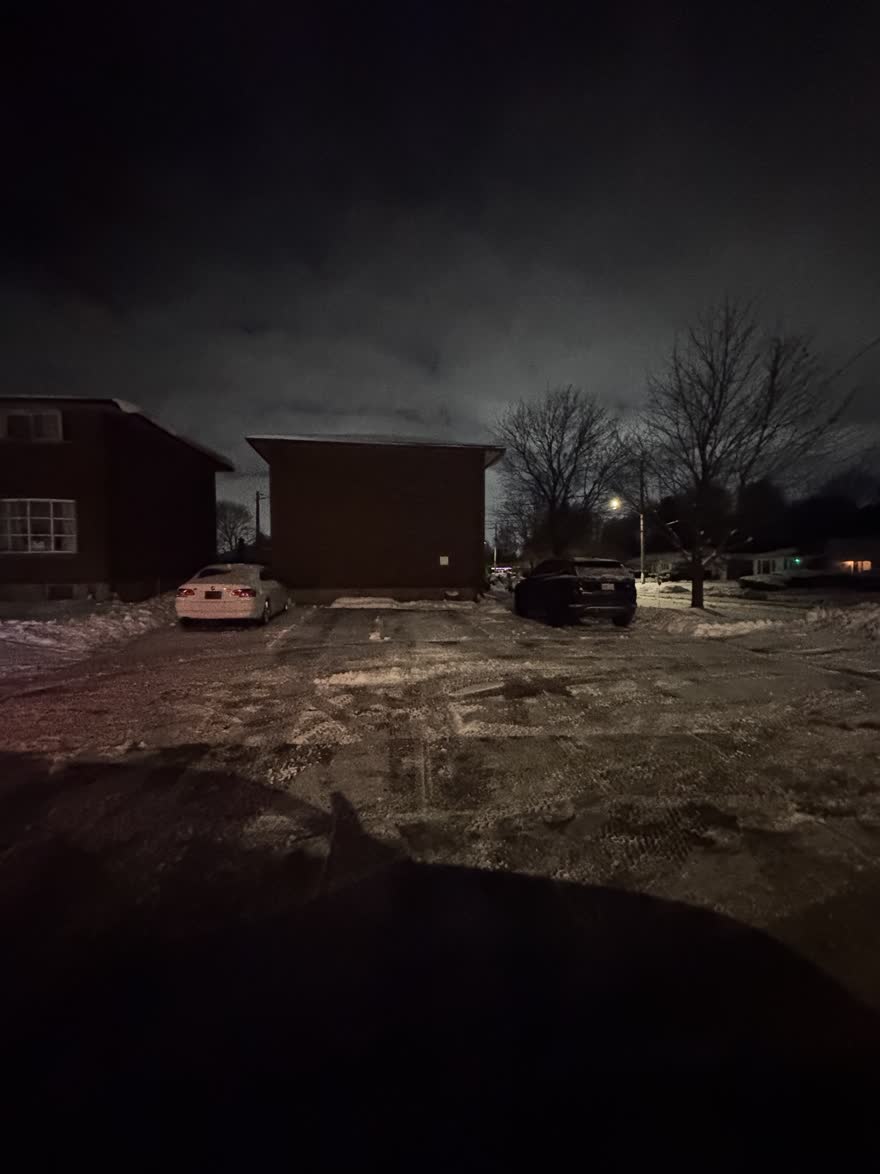 Small parking lot beside two buildings at night, plowed around two parked cars