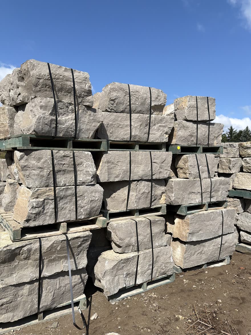 Pallets of large grey armour stone strapped and stacked at the stone yard